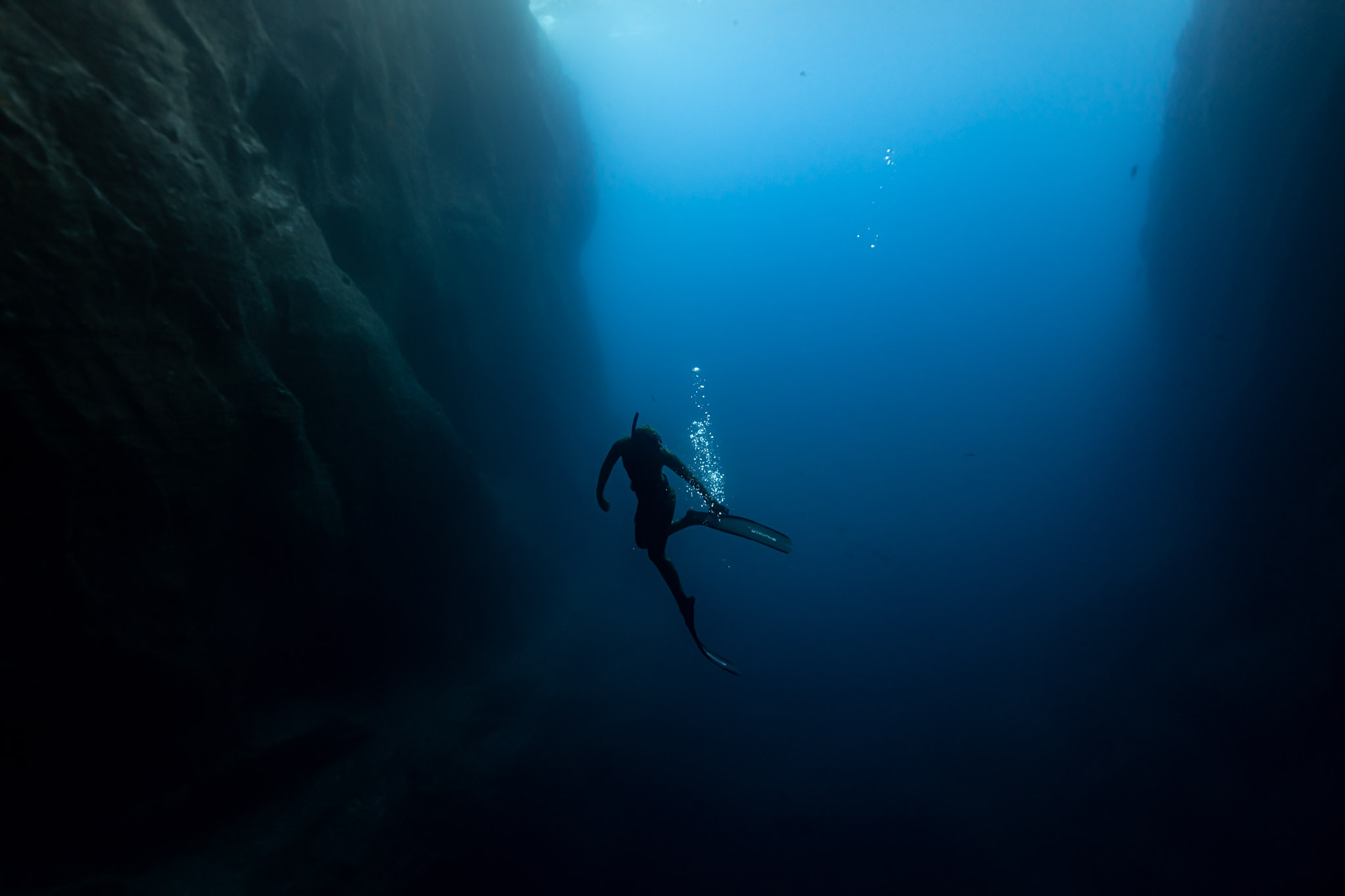 Freitaucher als Silhouette in einer Felsspalte vor den Azoren, Licht fällt von oben ins Wasser