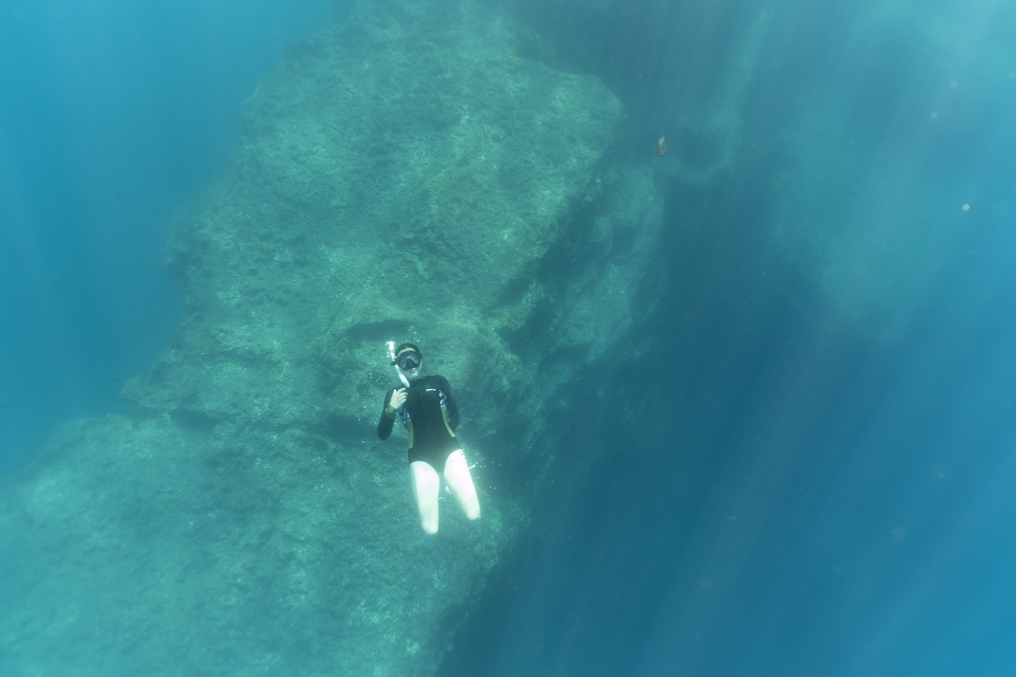 Freitauchende Person vor einer Felswand, das Wasser wirkt türkis-grün